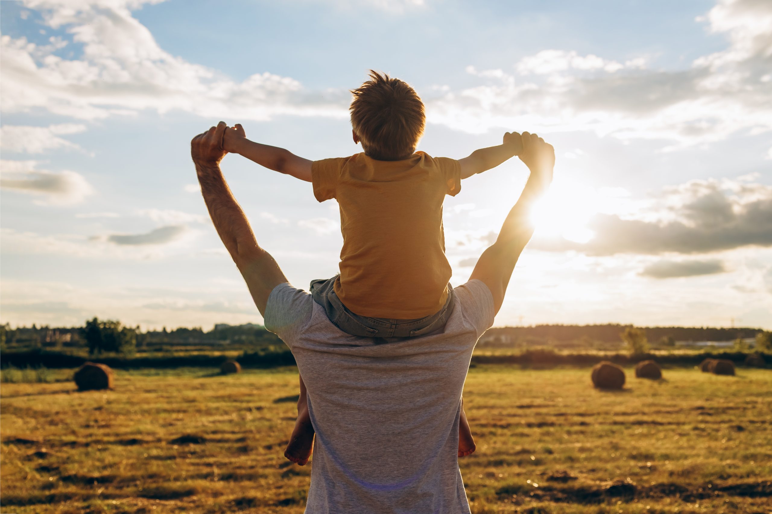 Father carrying child over open fields at sunset